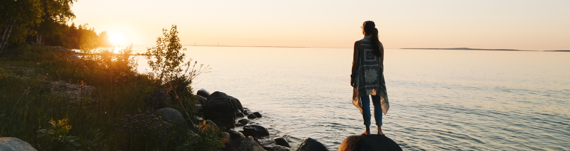 Woman pauses on lakeshore at sunrise, looks off
