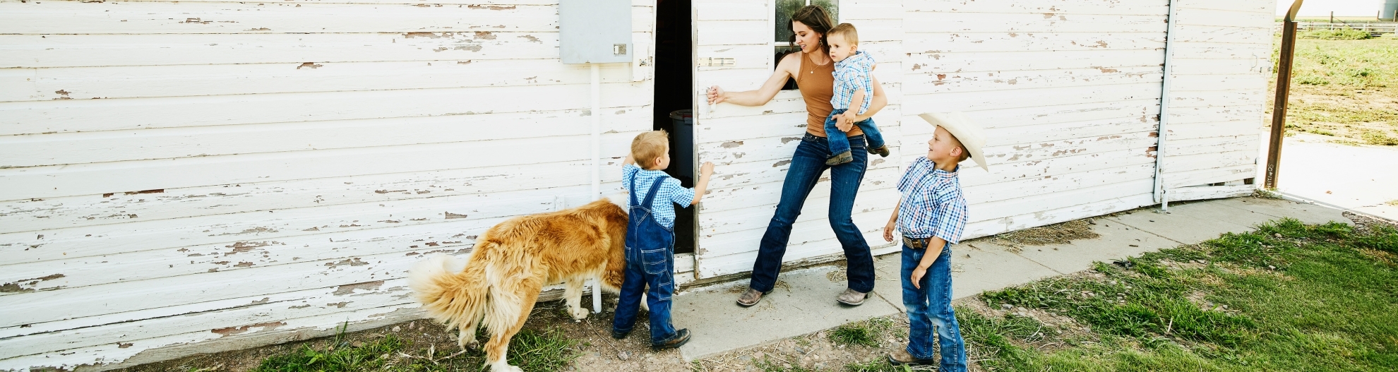 Wide shot of female farmer and young sons entering barn on farm